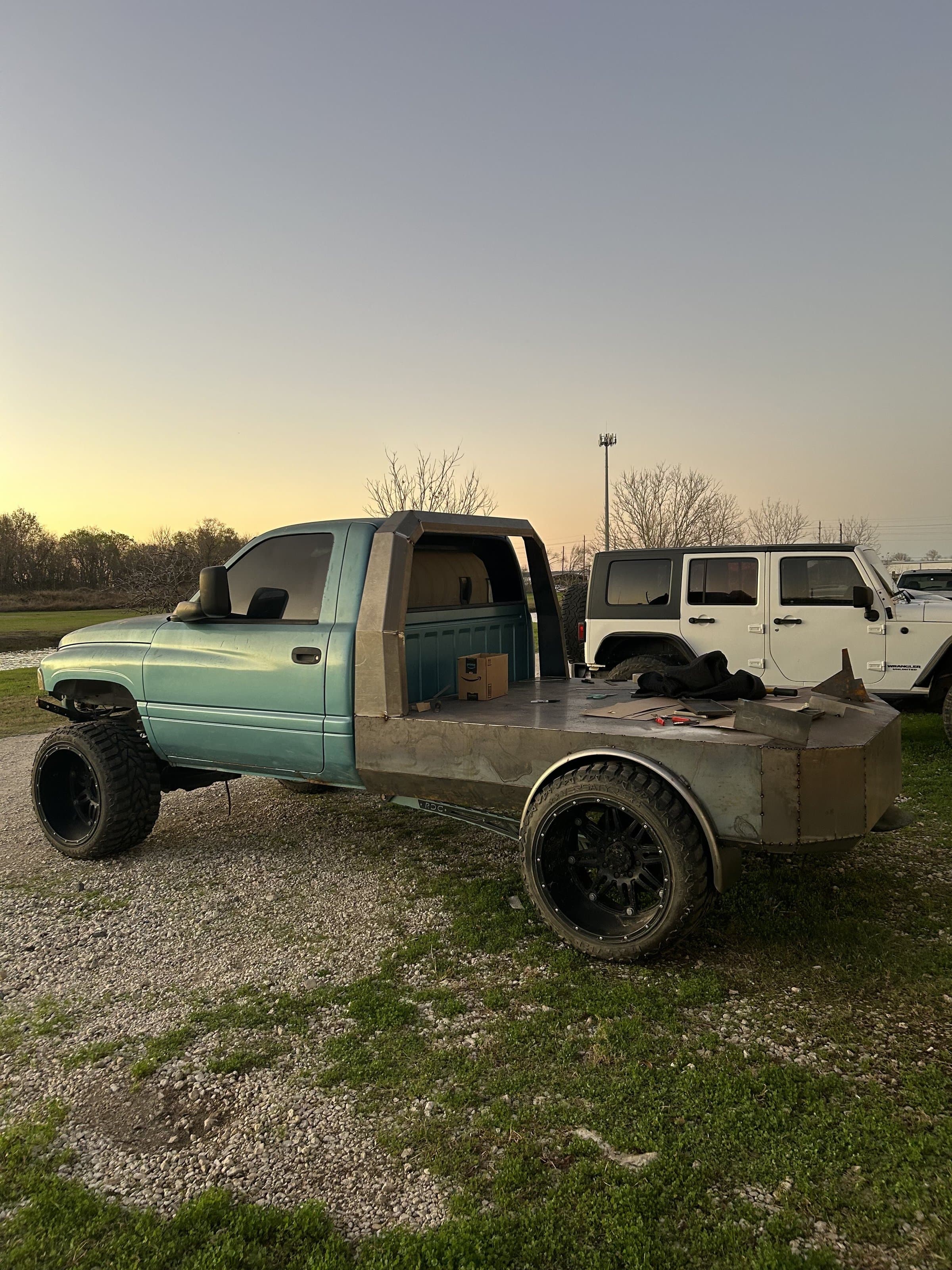 Custom raw steel flatbed with fabricated fender flares built in-house by 2 Man Fab on a lifted Dodge Ram, parked at the shop in Little Elm, TX at sunset