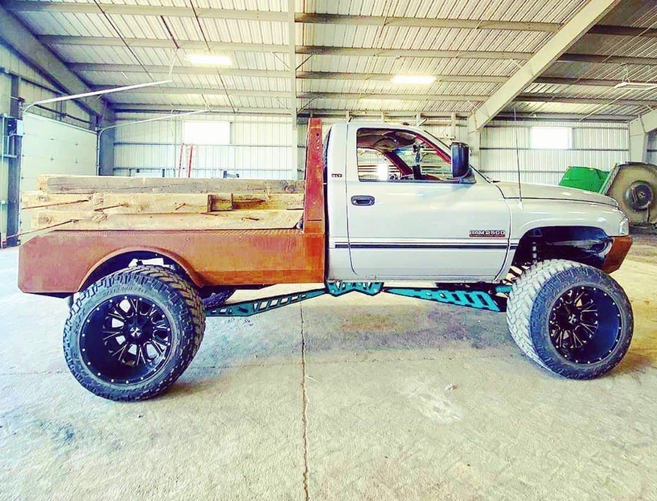 Second-gen Dodge Ram 2500 with a custom raw steel flatbed, parked inside the 2 Man Fab shop